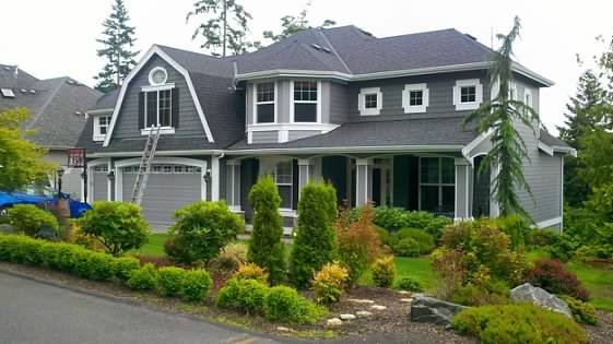 Large gray home with white trim and gambrel gables, photographed on the job