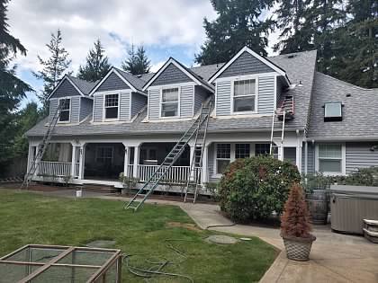 White two-story home with dormers, ladders in place during painting